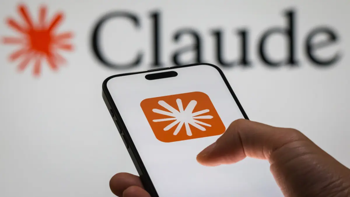 スマートフォンの画面に表示されたオレンジ色のアイコンを指で操作する手と、背景にぼやけて見えるロゴのイラスト風写真