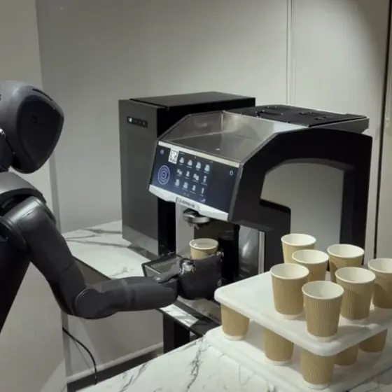 コーヒーマシンの前でカップを操作するヒューマノイドロボットの写真