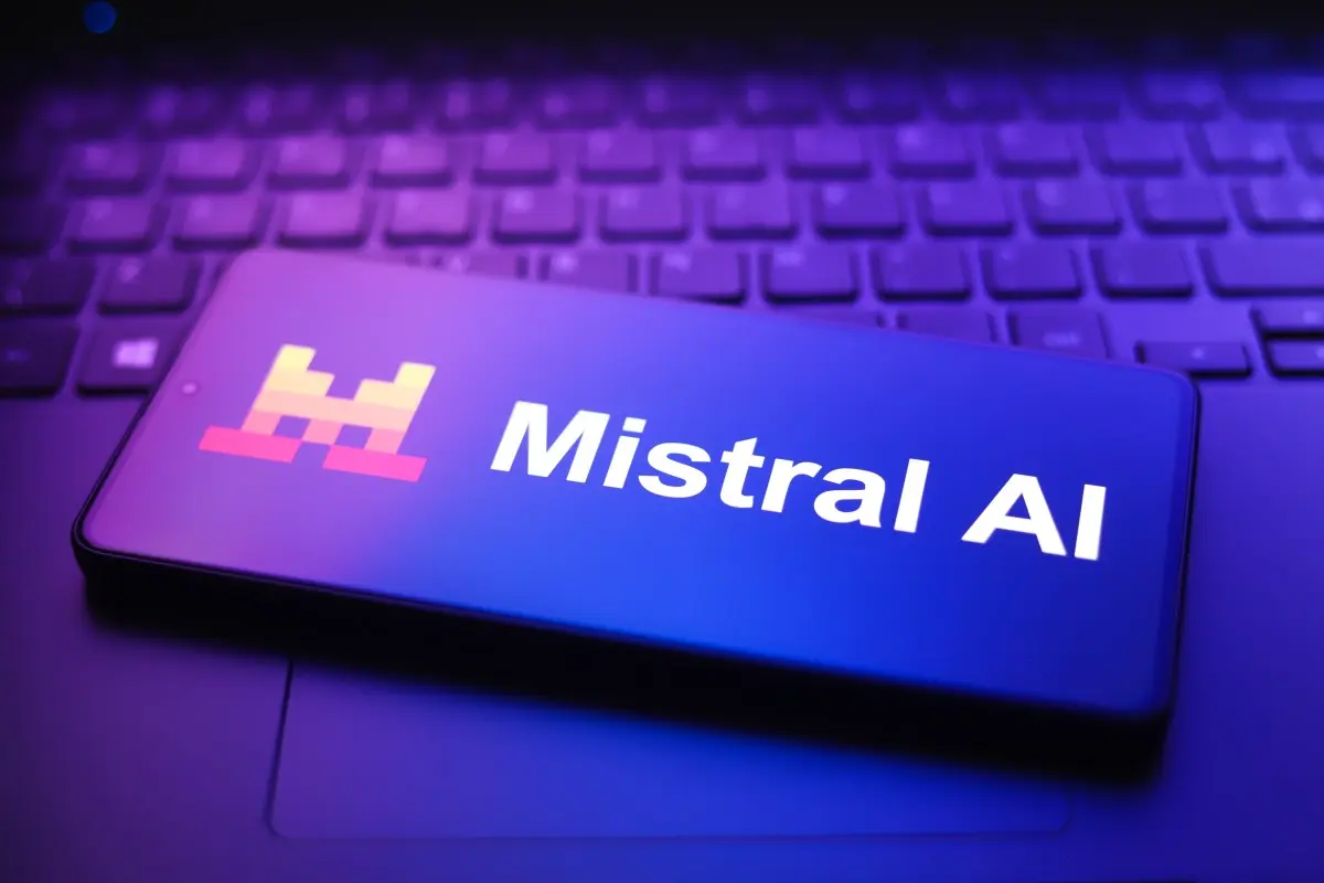 スマートフォンの画面に表示された「Mistral AI」のロゴとテキスト。紫と青の光を受けたノートパソコンのキーボードの上に置かれている