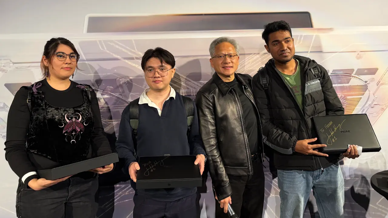 黒革ジャケットの男性と3人の参加者が、サイン入りのノートPCを手に記念撮影に収まっている様子