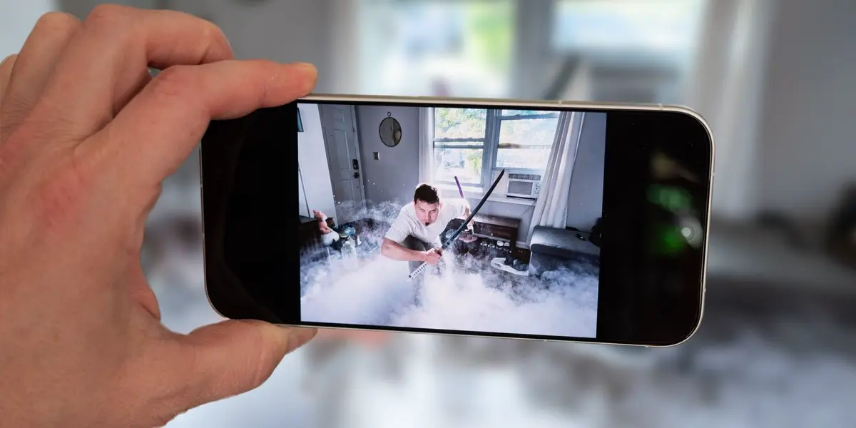 手に持ったスマートフォンの画面に白い煙の中で刀を構える人物を写したドラマチックな写真が表示されている様子